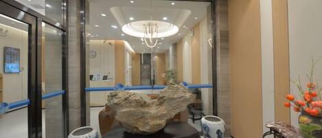 A hotel lobby with a reception desk, a chandelier, and a decorative rock centerpiece.