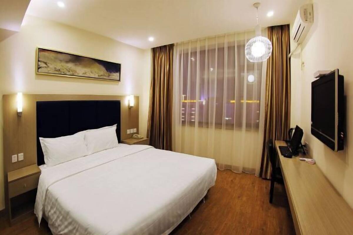 A hotel room with a bed, a desk, a TV, and a window with curtains.