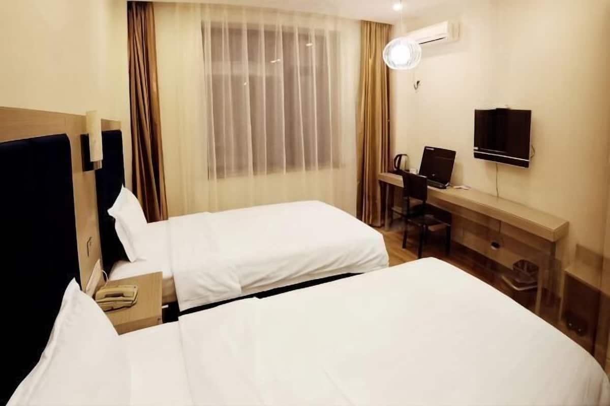 A hotel room with two beds, a desk with a chair, a television, and a window with curtains.