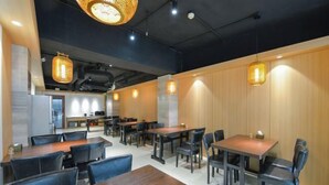 A modern dining area with wooden tables and chairs, pendant lighting, and a kitchen in the background. - Tianhe Express Hotel (Shenyang Middle Street Forbidden City) (Shenyang)