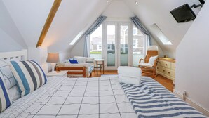 A cozy, well-lit attic bedroom with a bed, a chair, a small table, and a TV mounted on the wall.