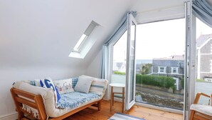 A cozy room with a wooden sofa, a small table, and a view of the street through large glass doors.