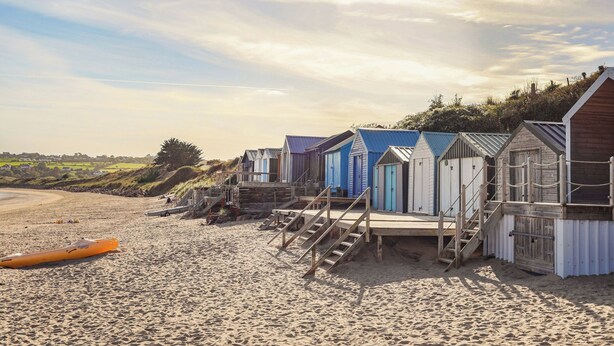 A row of beach huts with wooden stairs leading up to them, situated on a sandy beach.