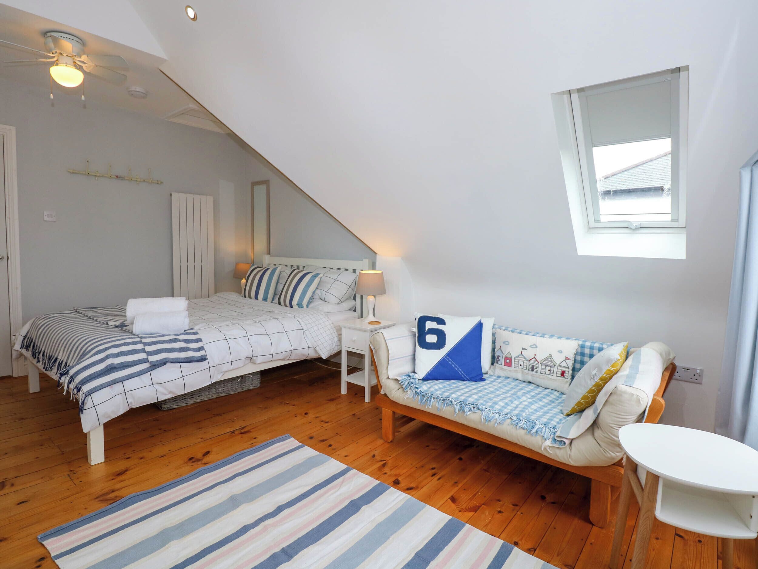 A bedroom with a bed, a sofa, a small table, a window, and a ceiling fan.