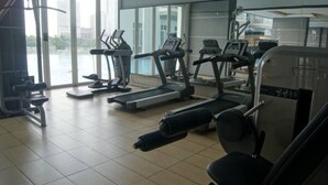 Une salle de sport équipée de tapis de course, d’appareils de musculation et d’une grande fenêtre donnant sur un plan d’eau.
