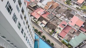 Un immeuble de grande hauteur, doté d’une piscine à sa base, est entouré d’un quartier densément peuplé, composé de différents bâtiments et bordé d’une rue.