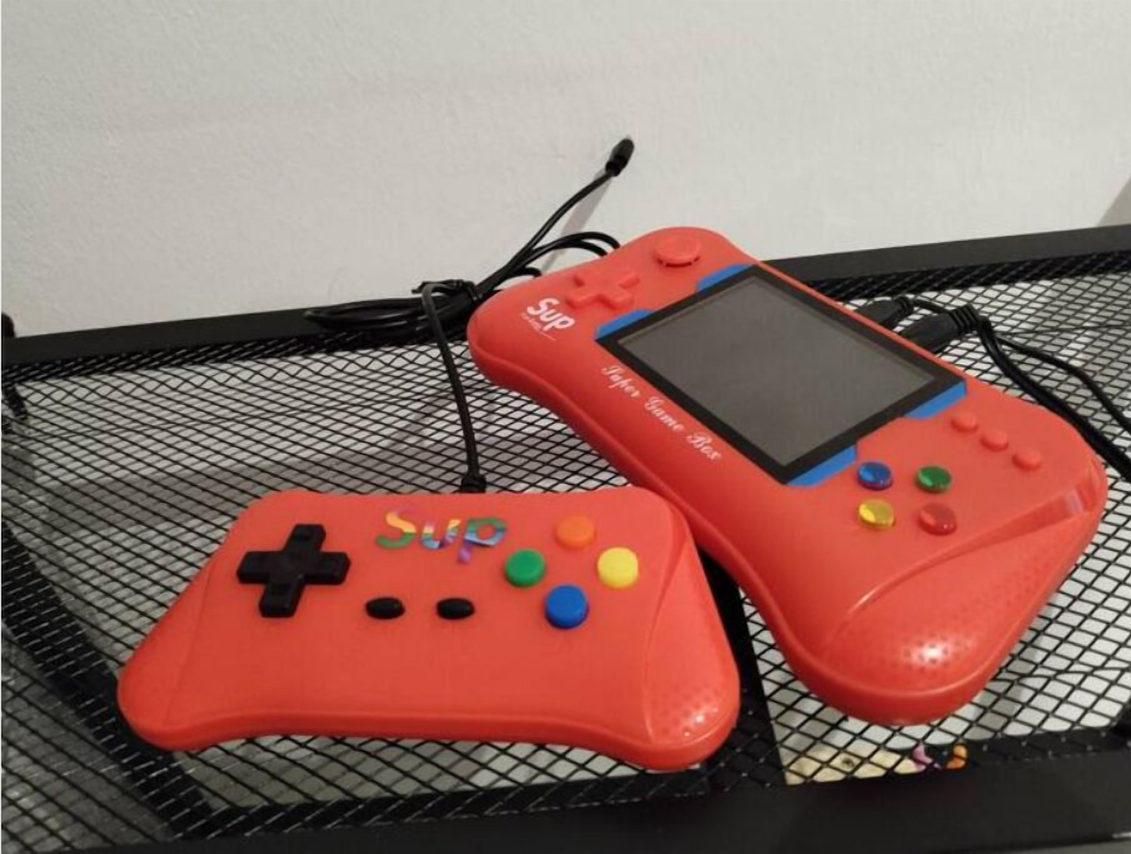 Two red game controllers on a black wire mesh surface.