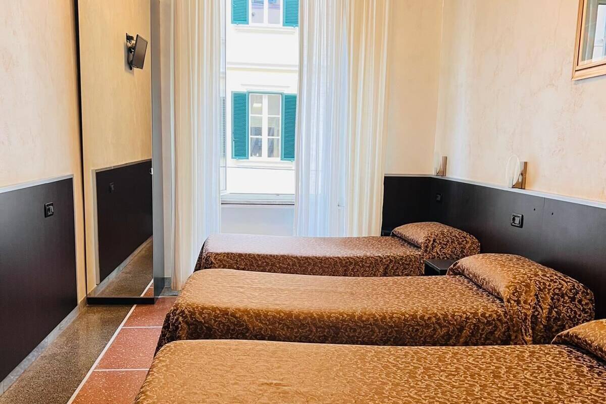 A hotel room with two beds, a door, a window with curtains, and a view of a building outside.