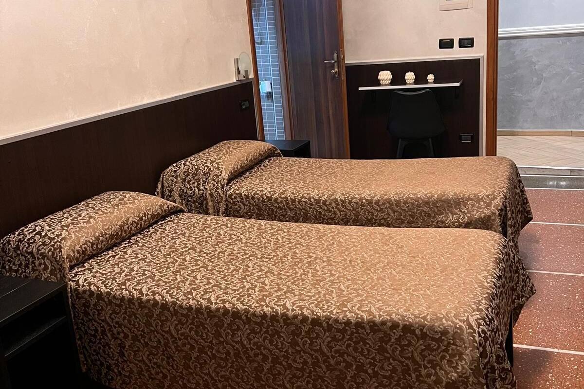 A hotel room with two beds, a painting on the wall, a desk with a chair, and a door leading to a balcony.