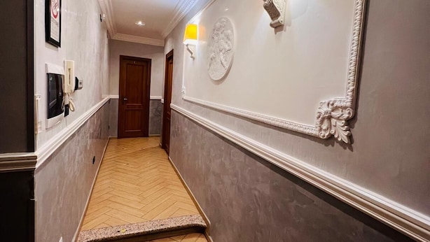 A hallway with a herringbone floor, a mirror with a decorative frame, and a wall-mounted light fixture. - FUNNY HOLIDAY ROME (Rome)