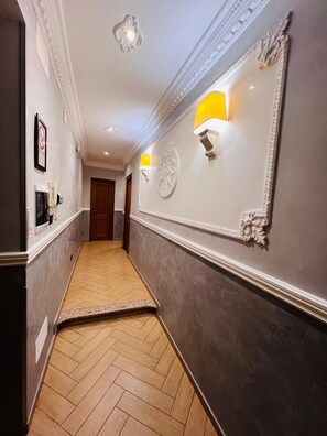 A hallway with a herringbone floor, a mirror with a decorative frame, and a wall-mounted light fixture. - FUNNY HOLIDAY ROME (Rome)