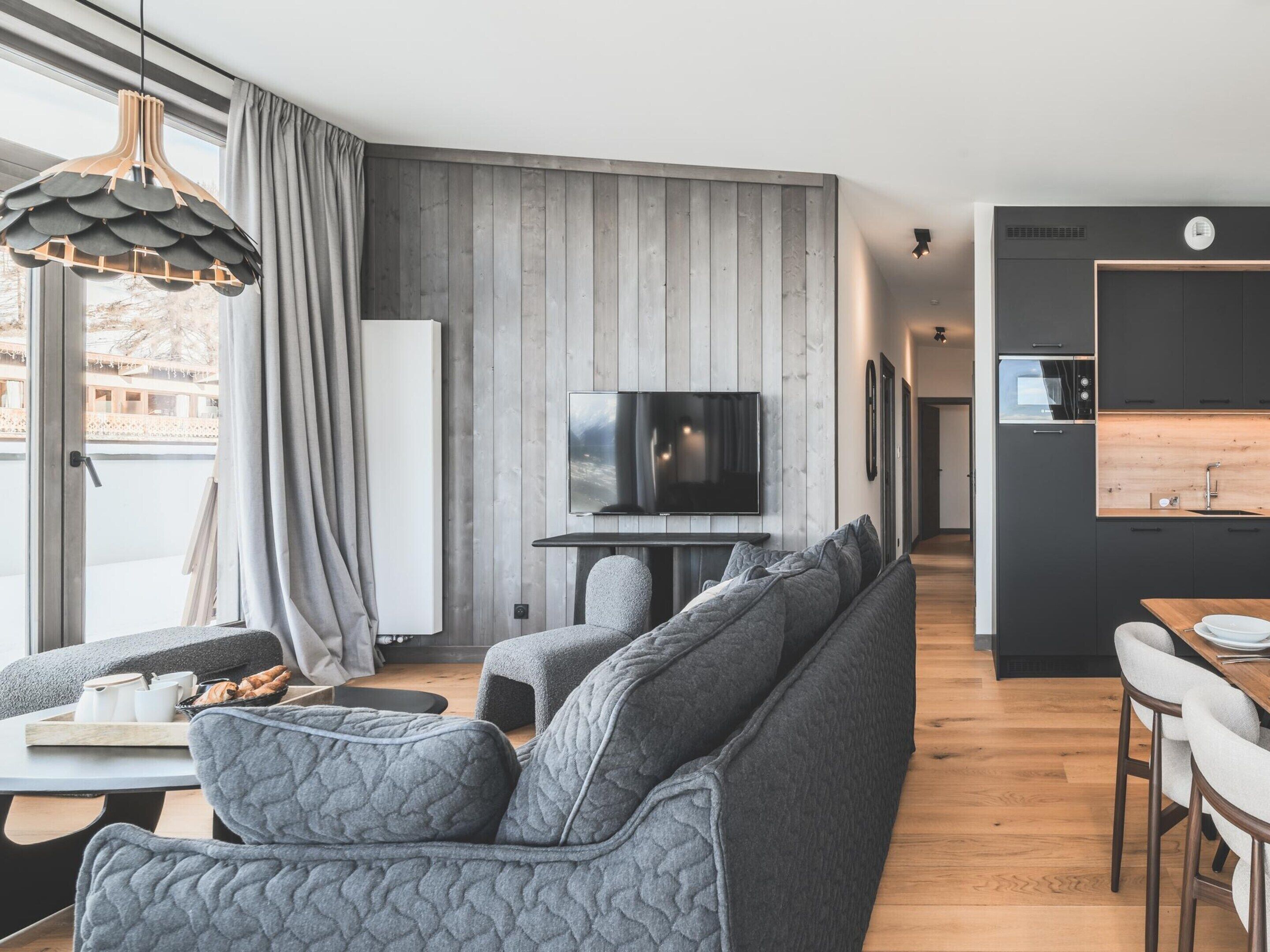Een moderne woonkamer met een grijze bank, een flatscreen televisie en een houten eettafel.