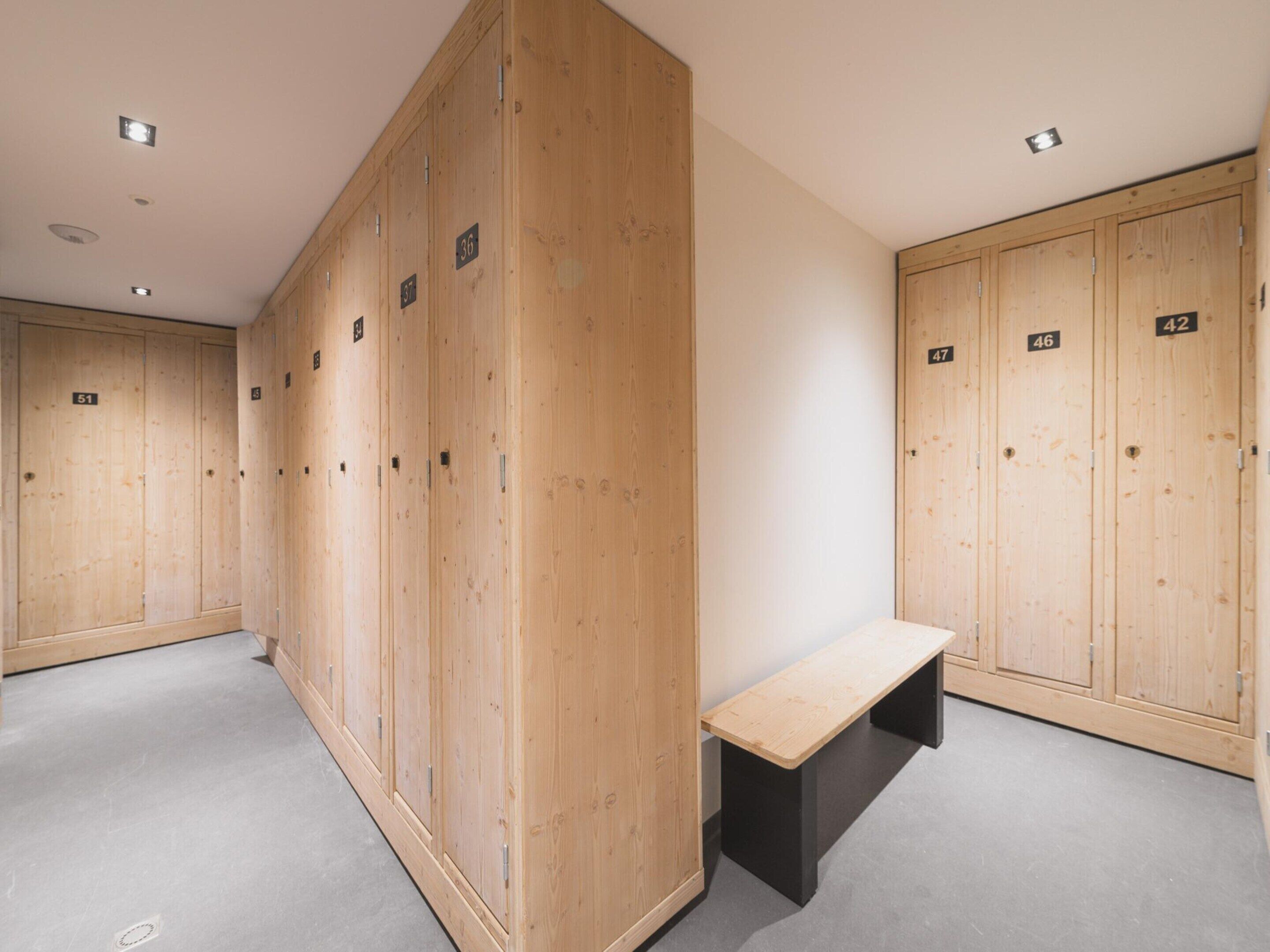 A row of wooden lockers with numbers, a bench, and a plain wall.