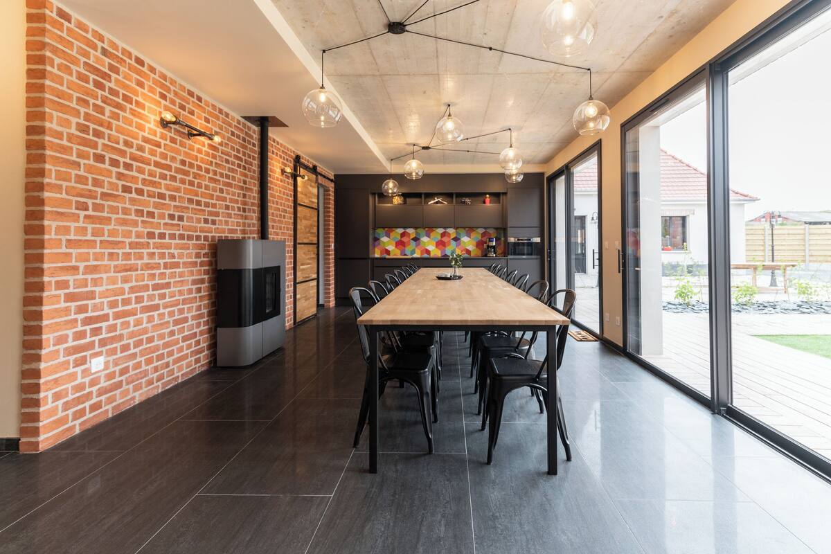 A modern dining area with a long table, black chairs, and pendant lighting.
