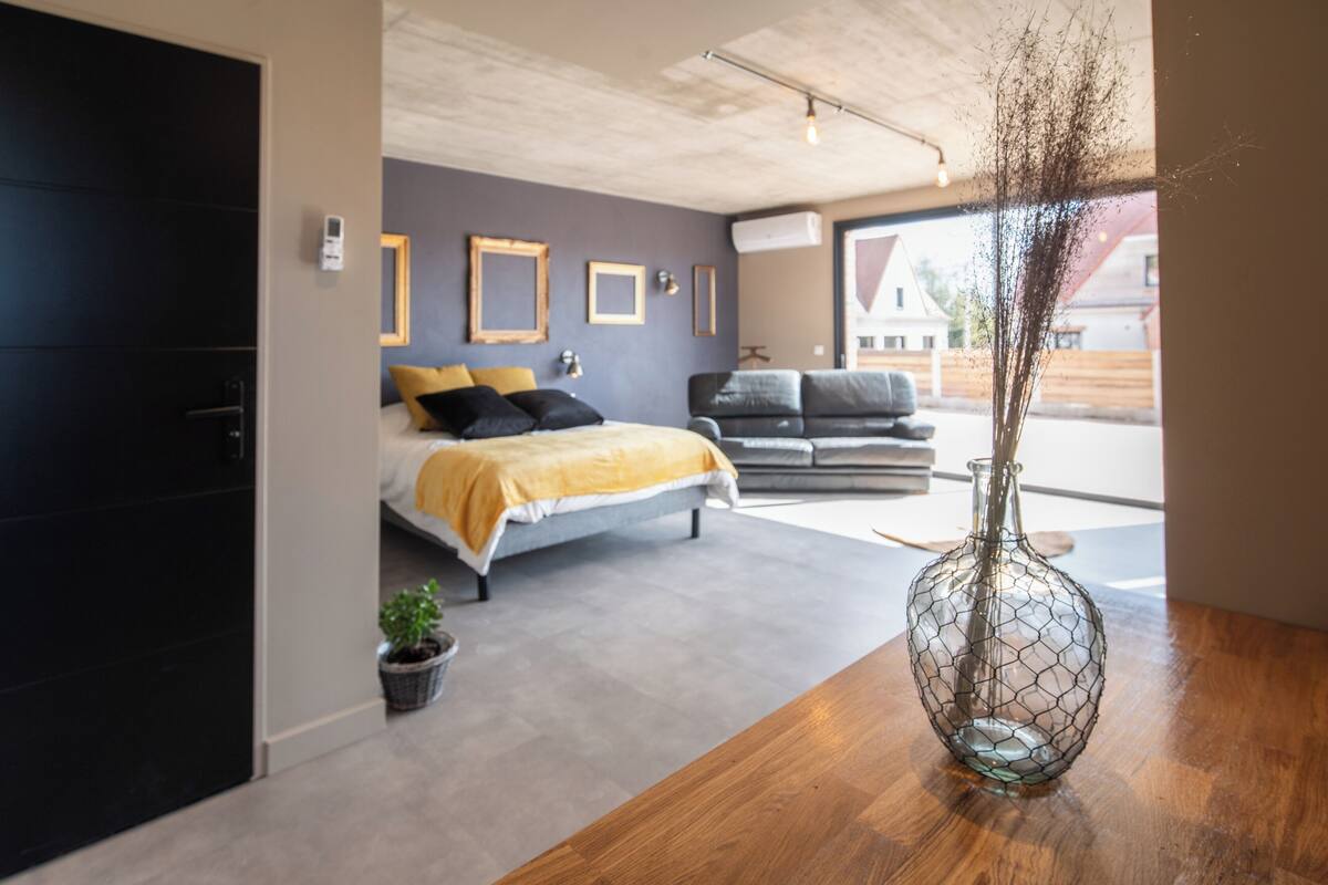 A modern bedroom with a bed, a sofa, a wooden table, and a vase.
