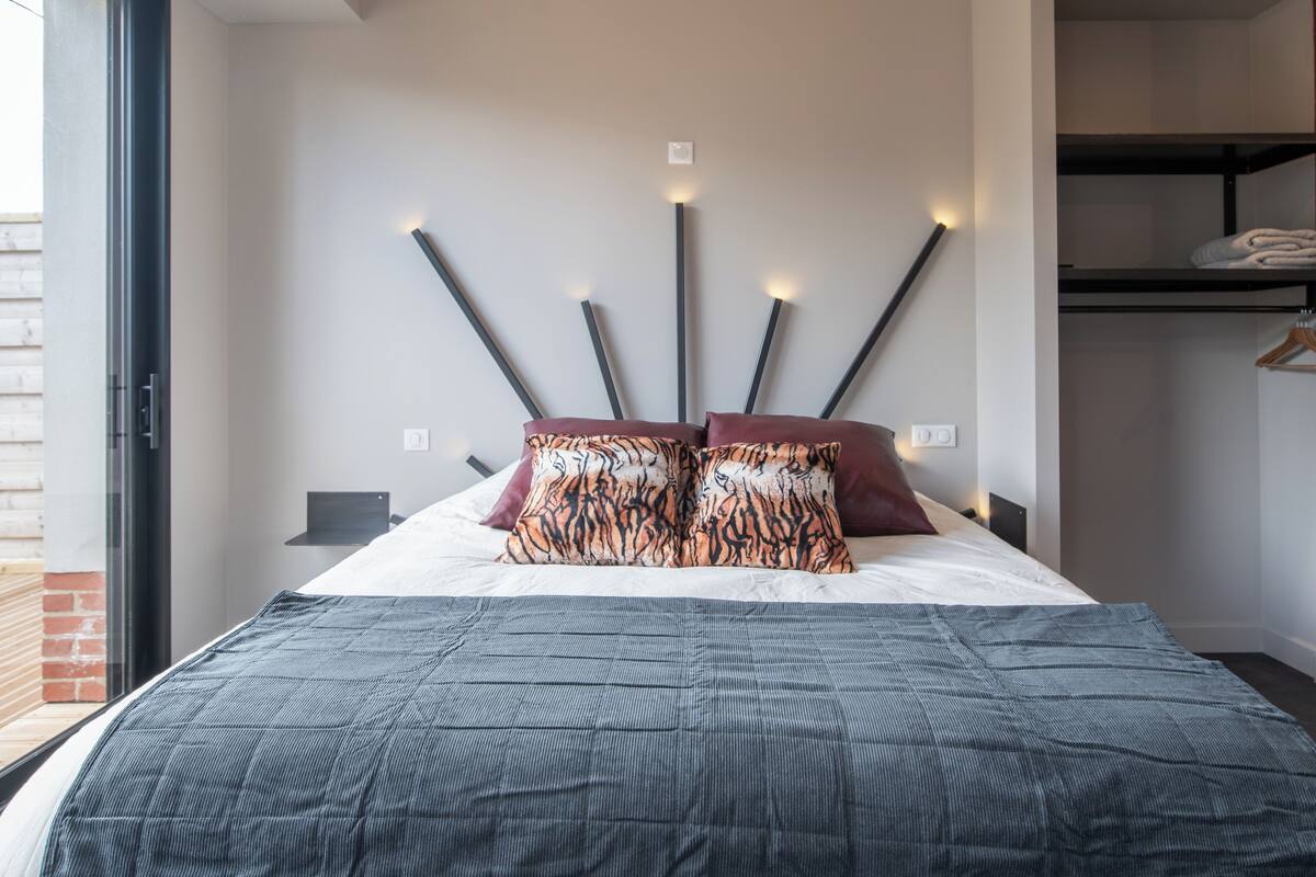 A modern bedroom with a large bed, a unique wall-mounted light fixture, and a view of a brick wall.