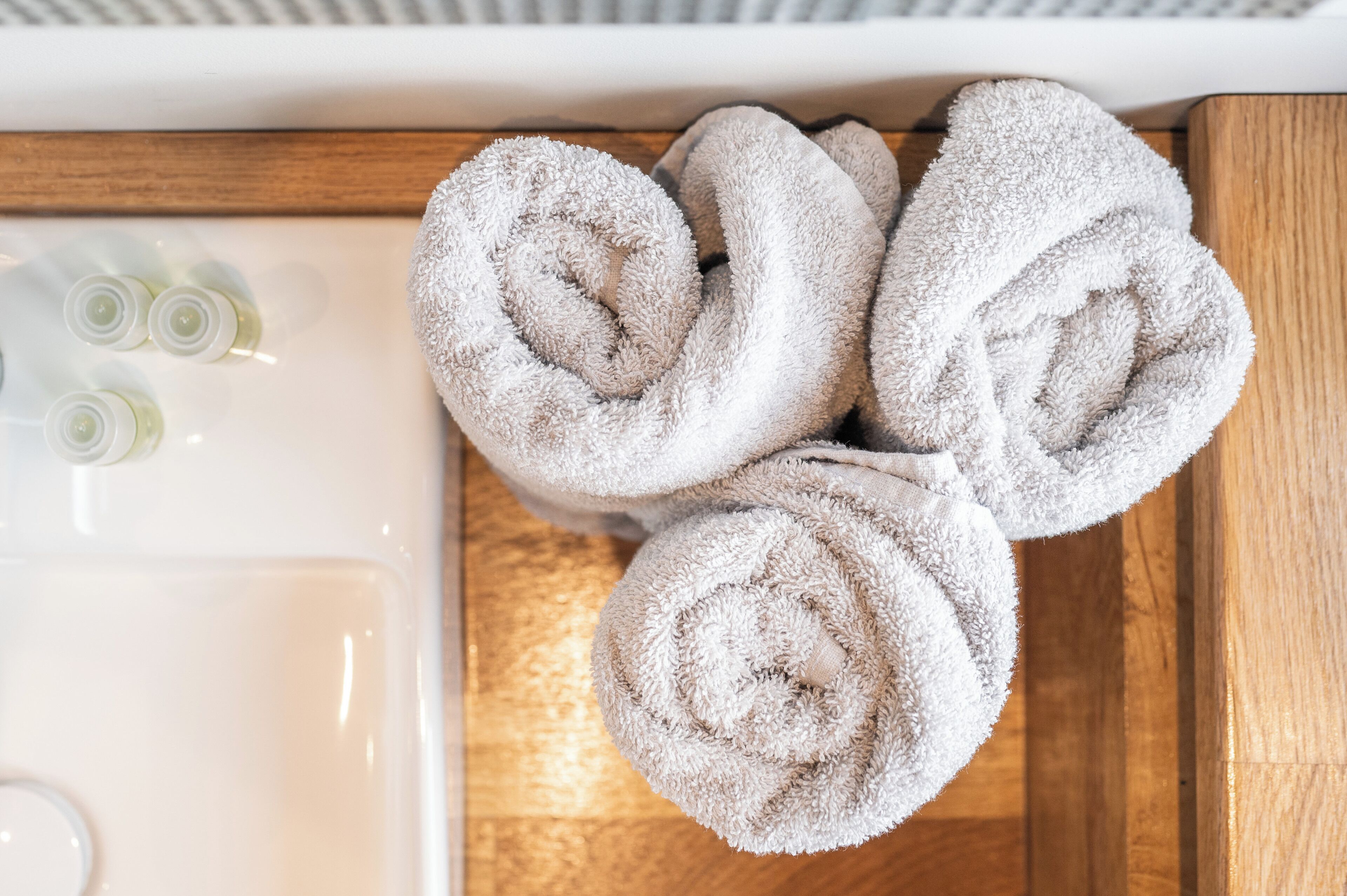 A bathroom with a wooden vanity, a sink, and three rolled towels.
