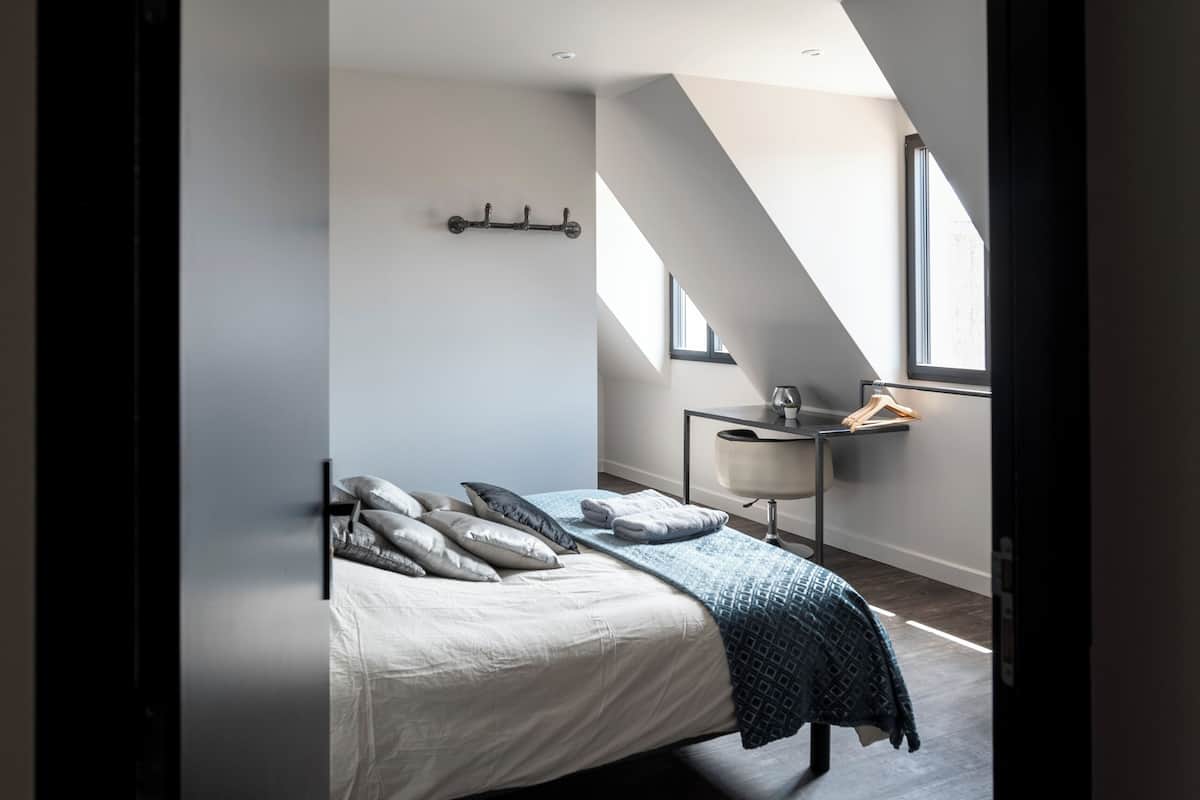 A bedroom with a bed, a nightstand, a desk, and a window.