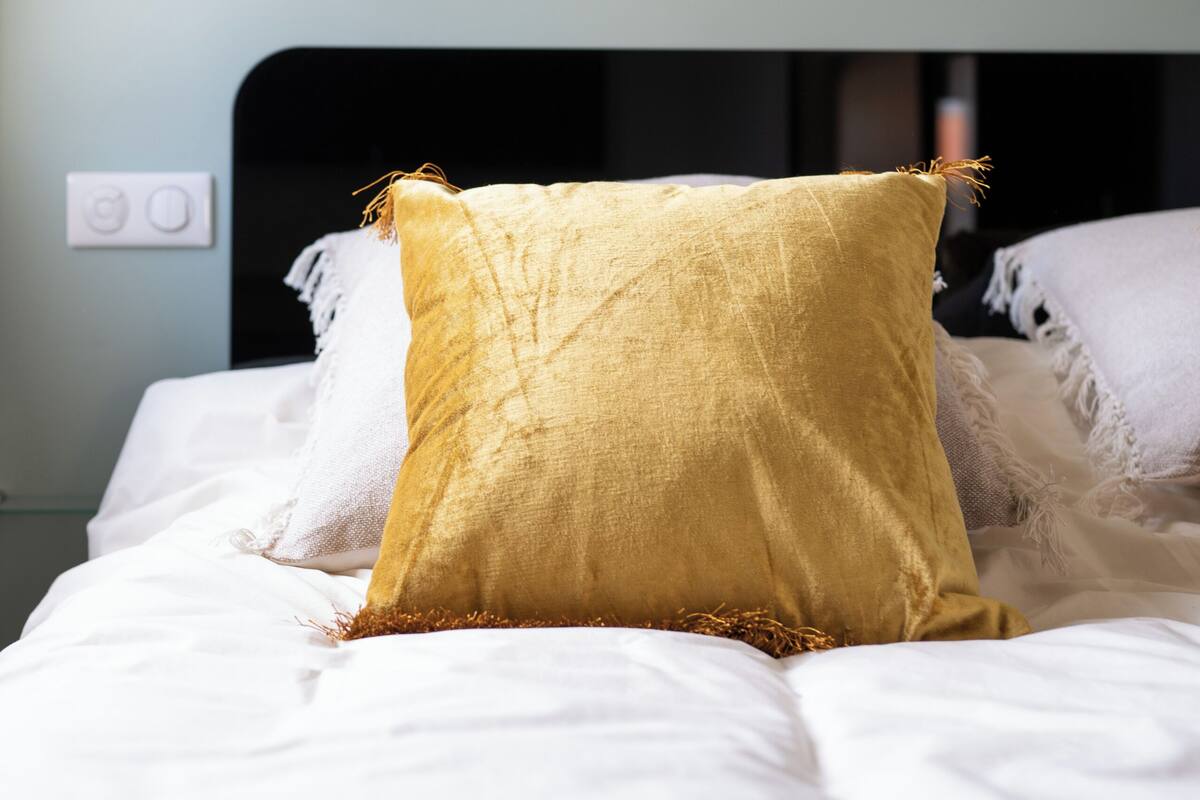 A bed with white bedding and a single yellow pillow.
