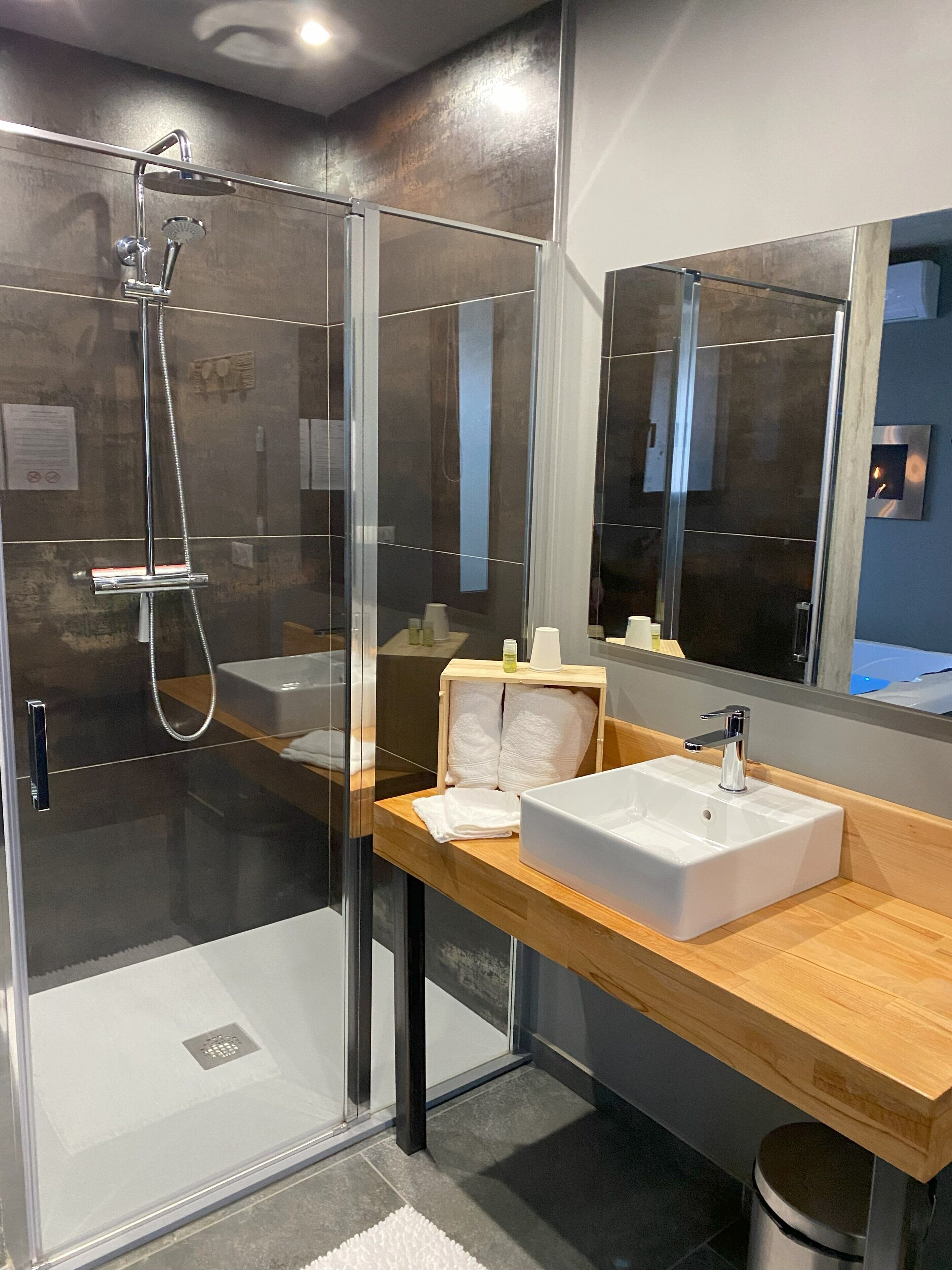A modern bathroom with a glass-enclosed shower, a wooden vanity with a white sink, and a large mirror.