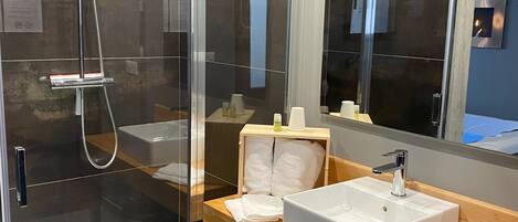 A modern bathroom with a glass-enclosed shower, a wooden vanity with a white sink, and a large mirror.