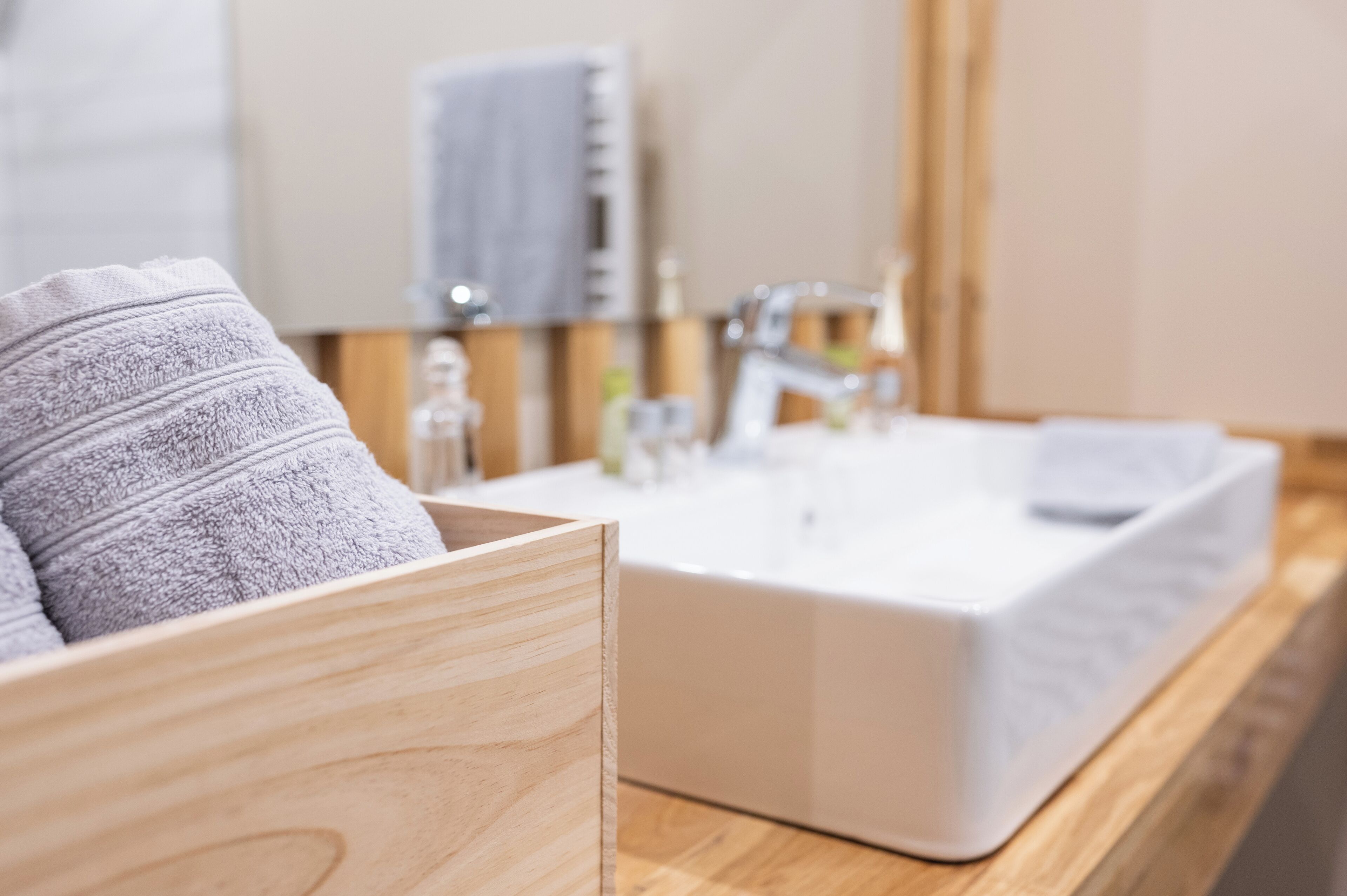 A modern bathroom with a wooden vanity, a white sink, and a towel hanging on the wall.