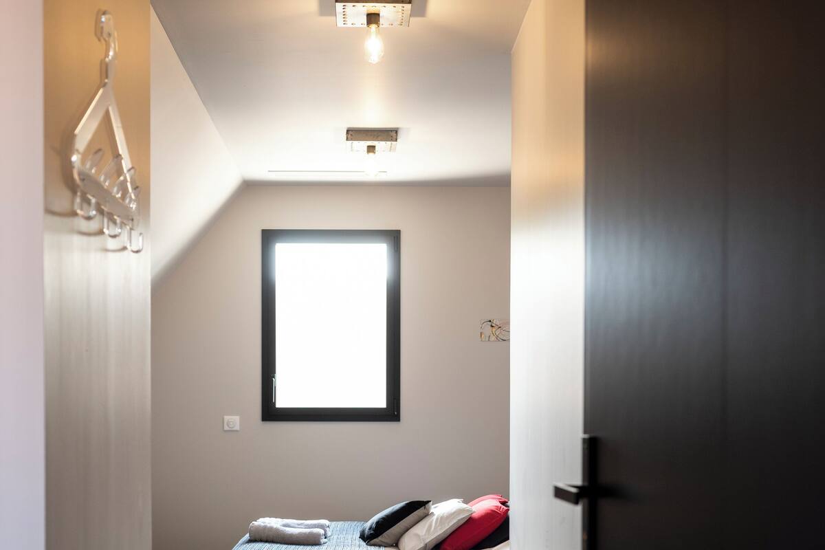 A narrow hallway leading to a bedroom with a bed, a window, and a door.