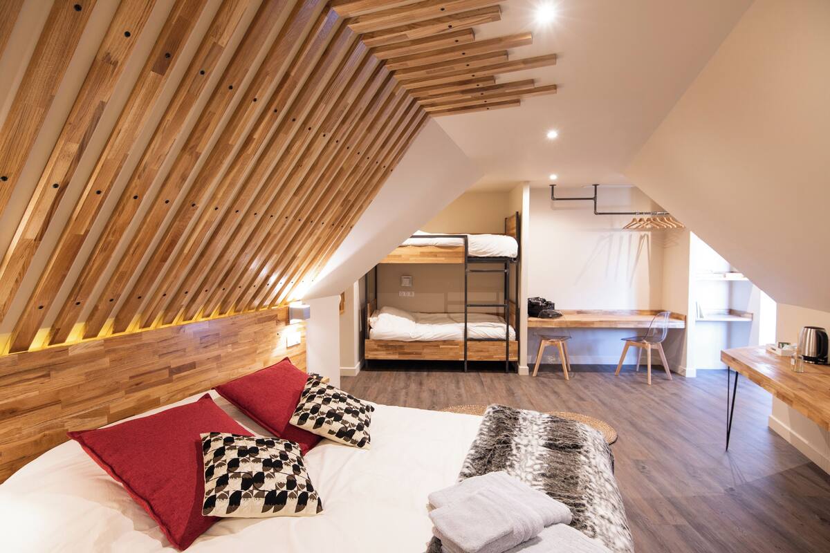 A modern, loft-style bedroom with a sloped ceiling, a bunk bed, a desk, and a comfortable seating area.