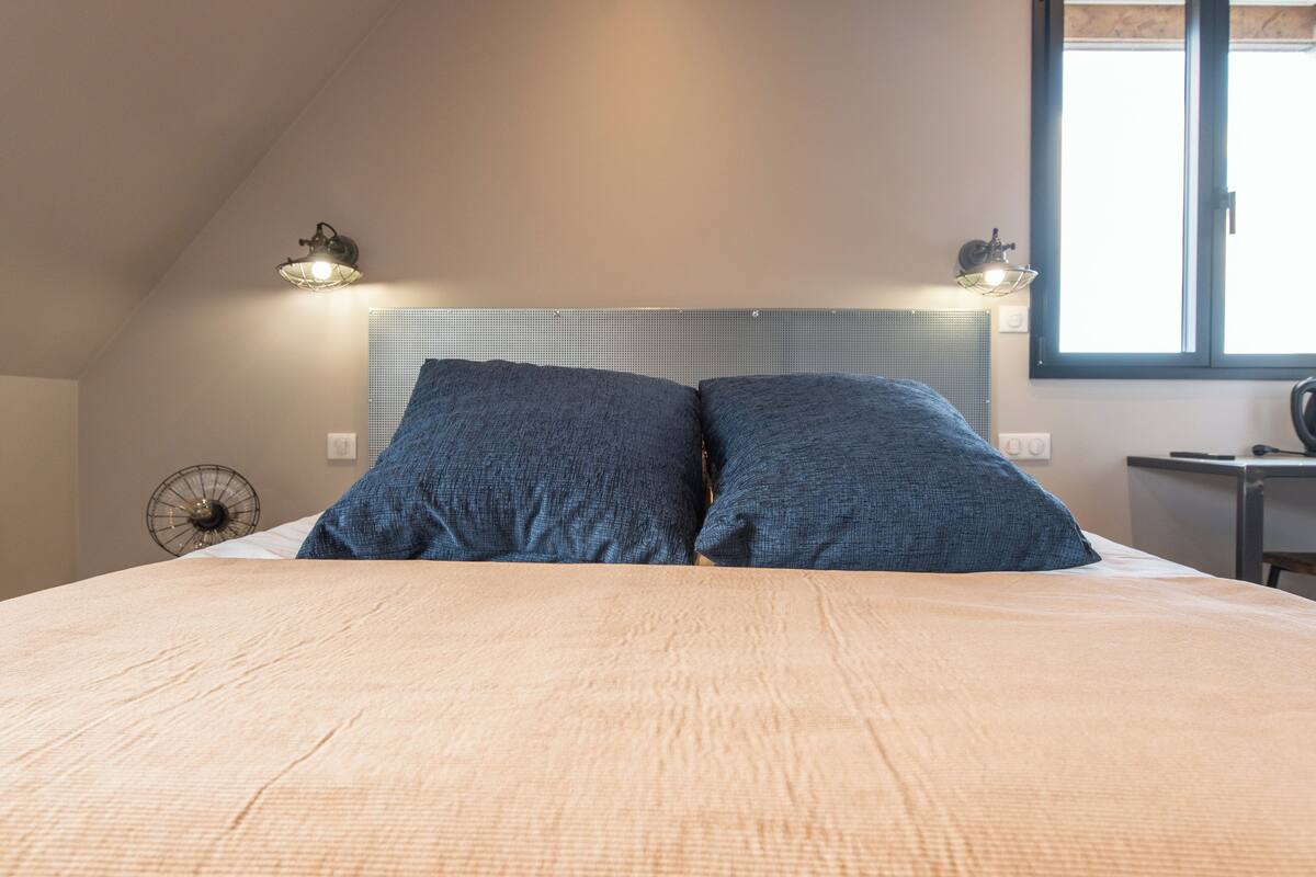 A bedroom with a large bed, two wall-mounted lamps, a ceiling fan, and a window with blinds.