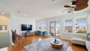 A spacious living room with a large flat-screen TV, a ceiling fan, and a balcony with sliding glass doors. - Villa Vilano |Summer by the beach! (St. Augustine Vilano Beach)