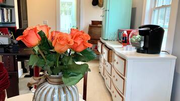 A kitchen with a white cabinet, a coffee maker, and a vase with orange roses.