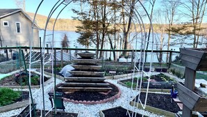 A garden with raised beds, a spiral staircase, and a view of a lake and trees. - Charming Grand View/Lake Loft in Brewster with WiFi, AC (Brewster)