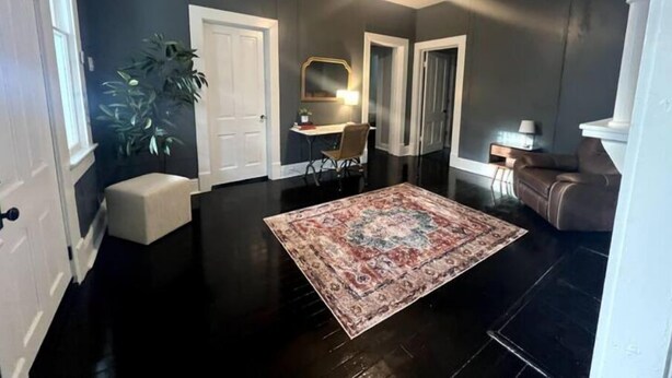 A spacious living room with a large dark wood floor, a patterned rug, a brown leather sofa, a white door, and a plant. - The Isabella - Beautifully Revived Historic House - 2 blocks from the IP Mill (Bogalusa)