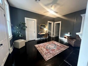A spacious living room with a large dark wood floor, a patterned rug, a brown leather sofa, a white door, and a plant. - The Isabella - Beautifully Revived Historic House - 2 blocks from the IP Mill (Bogalusa)