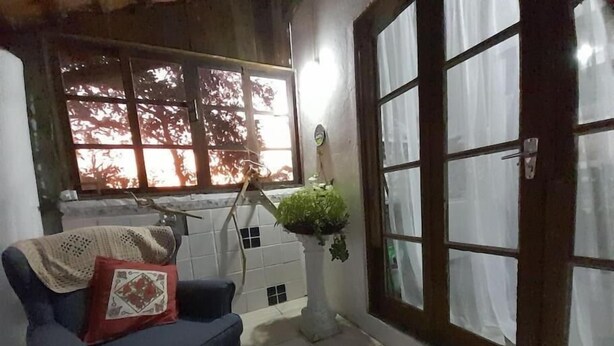 A cozy living room with a blue armchair, a small table, and a window with a view of trees. - Casa Jardim Secreto I (Penha)