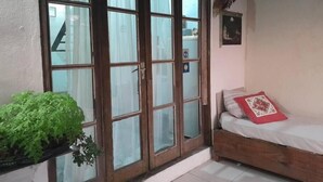 A room with a wooden bed, a small window with curtains, and a potted plant. - Casa Jardim Secreto I (Penha)