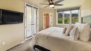 A bedroom with a bed, a ceiling fan, a TV, and a window with a view of greenery. - Terraces Condo w/ Stunning Views, Pool & Spa 1078 (Steamboat Springs)
