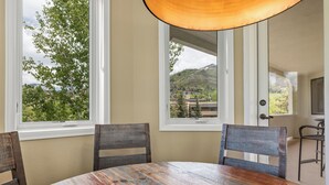 A dining area with a round wooden table, four chairs, and large windows offering a view of a mountainous landscape. - Terraces Condo w/ Stunning Views, Pool & Spa 1078 (Steamboat Springs)