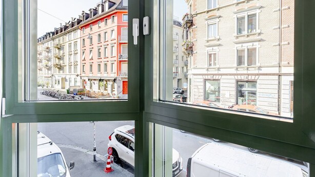 A view through a window of a street with parked cars and a row of colorful buildings.