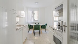 A modern kitchen with white cabinets, a granite countertop, and a built-in oven. There is a round table with green chairs in the center.