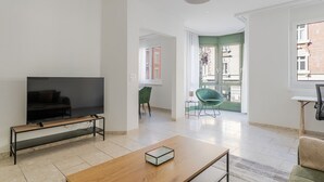 A modern living room with a flat-screen TV on a wooden stand, a green chair, and a wooden coffee table.