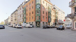 A multi-story building with a mix of residential and commercial spaces, featuring a variety of architectural styles and a parking area in front.