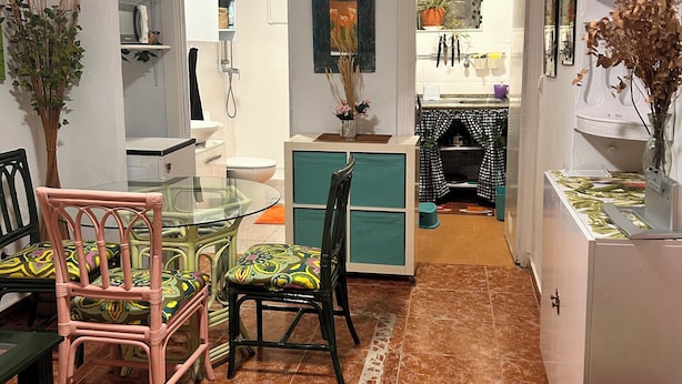 A compact kitchen with a dining area, featuring a glass-top table, chairs, and a small refrigerator.