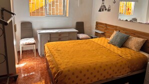 A bedroom with a bed, a desk, a chair, a wardrobe, and a window with a view of buildings.