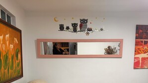 A living room with a beige sofa, a small black coffee table, a mirror with a pink frame, and a wall decoration of owls and stars.