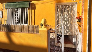 A yellow building with a number 33, a window with a green awning, a wooden fence, and a decorative bollard.