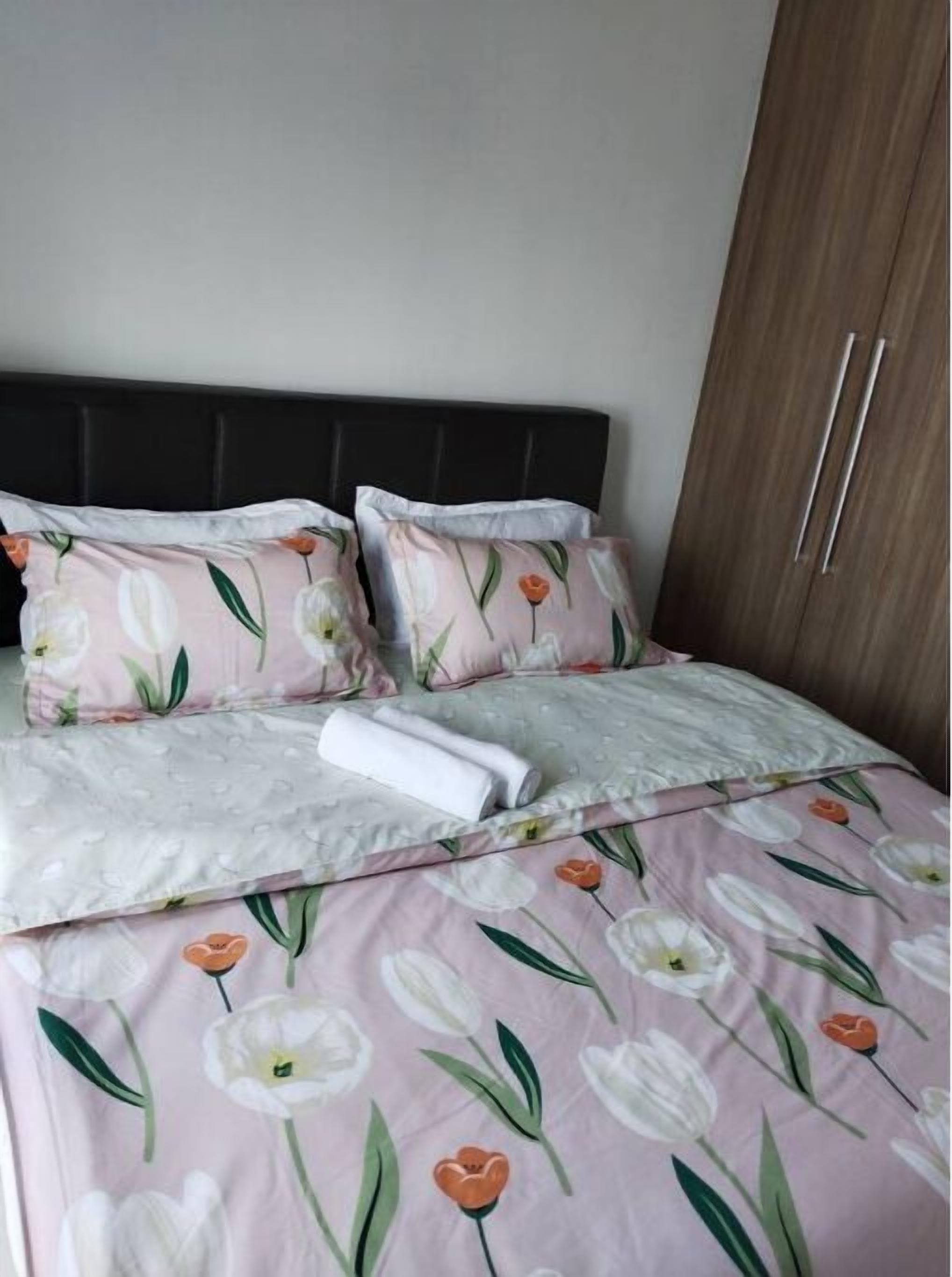 A neatly made bed with floral bedding, a dark headboard, and a wooden wardrobe with two doors.