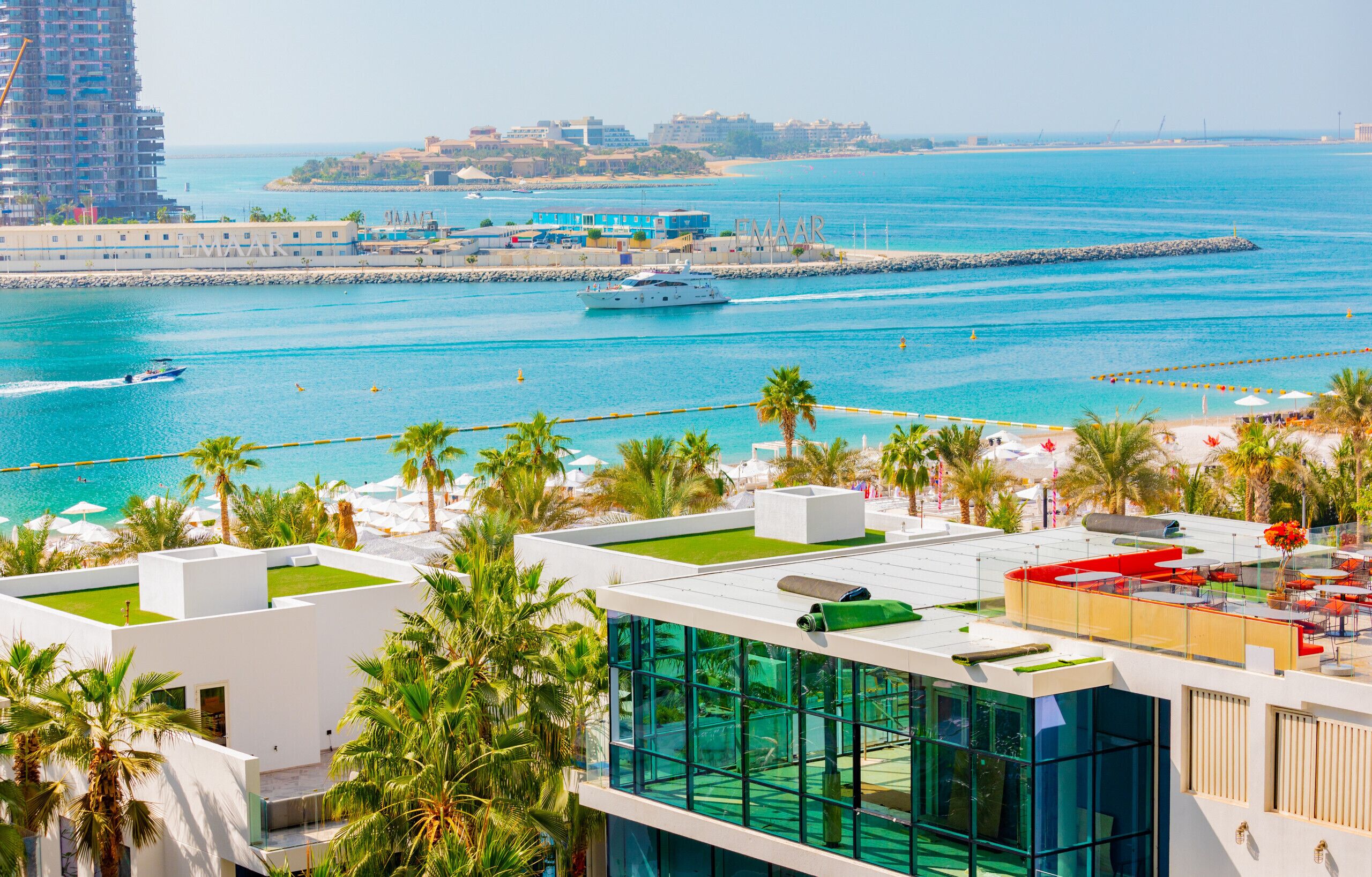 Une terrasse sur le toit avec une piscine, des palmiers et une vue sur la mer et les bâtiments.