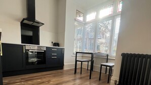 A modern kitchen with a built-in oven, a black range hood, and a dining area with a chair and table. - The Cube hidden gem in the heart of ilfracombe , 2 minute walk to tunnels beach! (Ilfracombe)