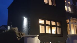 A two-story house with a dark exterior, illuminated windows, and a gated entrance. - The Cube hidden gem in the heart of ilfracombe , 2 minute walk to tunnels beach! (Ilfracombe)